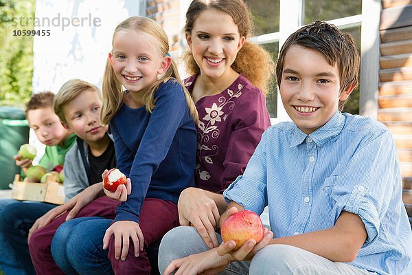 Porträt von Teenagern und Kindern  die auf der Terrasse sitzen und Äpfel essen.