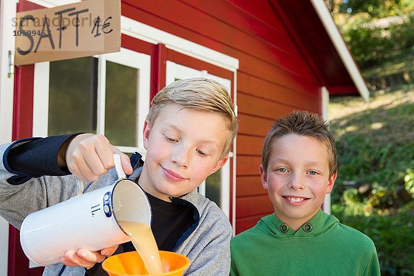 Zwei Brüder gießen frischen Orangensaft  um ihn am Straßenrand zu verkaufen.