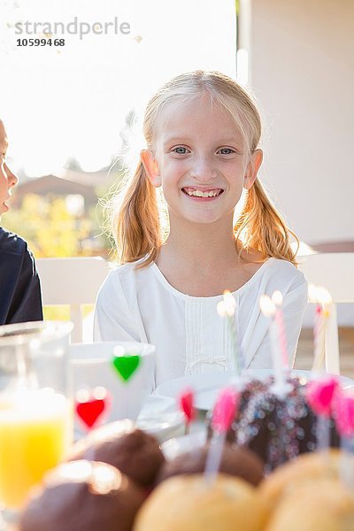 Porträt eines glücklichen Mädchens mit Geburtstagskuchen am Terrassentisch