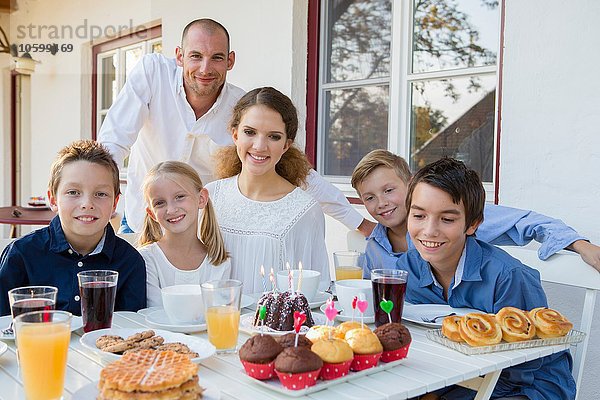 Porträt eines erwachsenen Mannes und einer Familie mit Geburtstagskuchen am Tisch auf der Terrasse