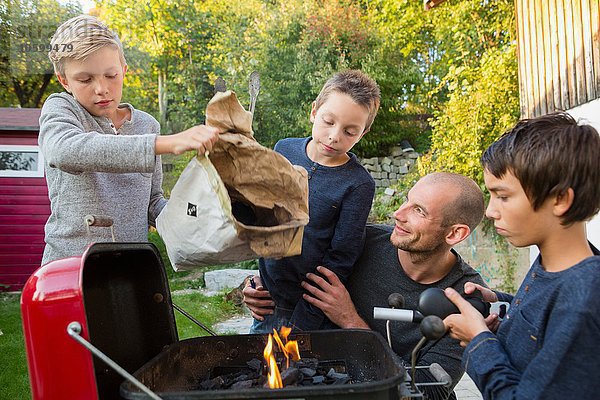 Mittlerer Erwachsener Mann und Söhne beim Grillen im Garten