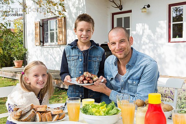 Porträt von Vater und Kindern am Gartengrilltisch