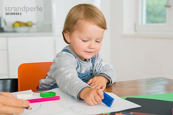 Kleinkind mit Radiergummi beim Zeichnen am Küchentisch