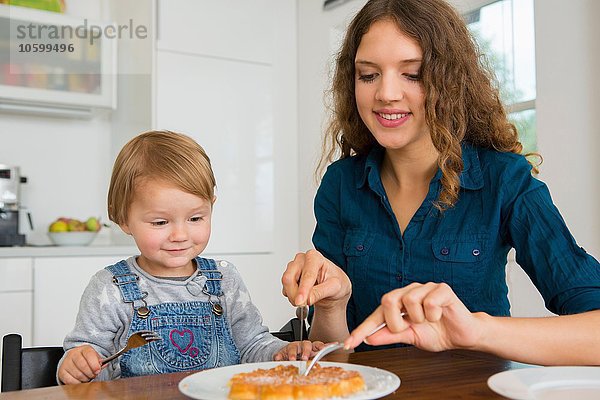 Teenager Mädchen schneidet Kuchen für weibliche Kleinkinder am Küchentisch