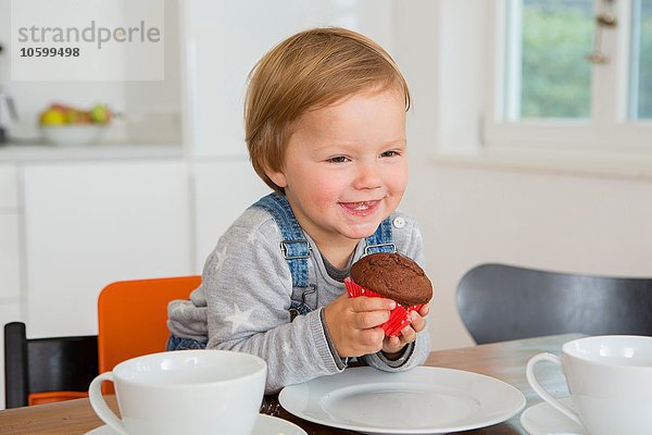 Süßes weibliches Kleinkind mit Muffin am Küchentisch