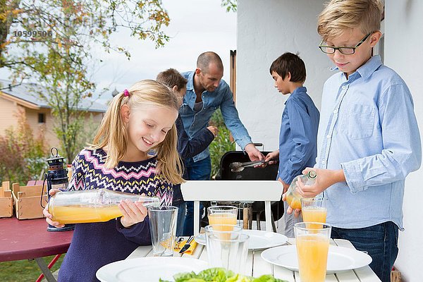 Mädchen und Bruder giessen Saft am Gartengrilltisch