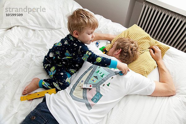 Junge spielt mit Spielzeugauto auf dem Rücken des Vaters T-Shirt im Bett
