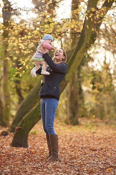 Mittlere erwachsene Frau hält Baby-Tochter im Herbstpark hoch