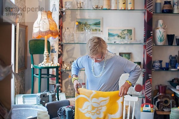 Reife Frau faltet gelbe Decke im Vintage-Shop