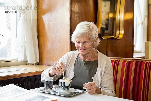 Seniorin im Café sitzend  Kaffee rührend