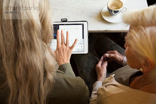 Mutter und Tochter sitzen zusammen im Cafe  Blick auf digitales Tablett  Rückansicht