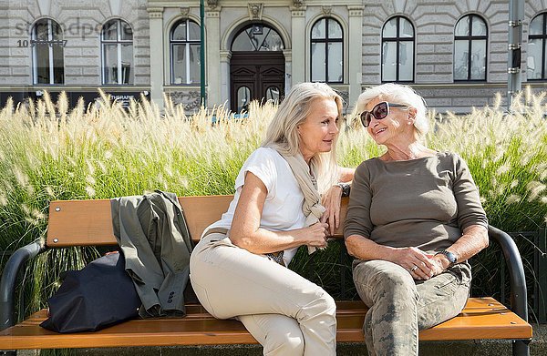 Mutter und Tochter sitzen gemeinsam auf der Bank  im Freien