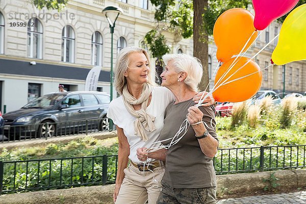 Mutter und Tochter gehen zusammen die Straße entlang und halten einen Haufen Ballons.