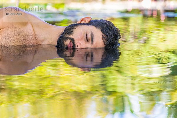 Bärtiger junger Mann im Wasser liegend  Illusion eines Spiegelbildes  Taiba  Ceara  Brasilien
