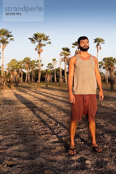Vorderansicht des jungen Mannes  der vor Palmen steht und Schatten wirft  Taiba  Ceara  Brasilien