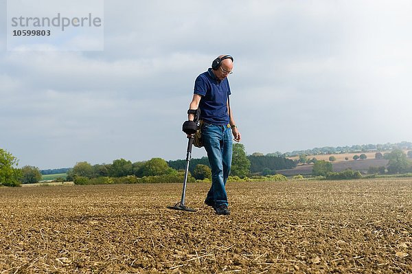 Reifer Mann mit Kopfhörer sucht schlammiges Feld mit Metalldetektor