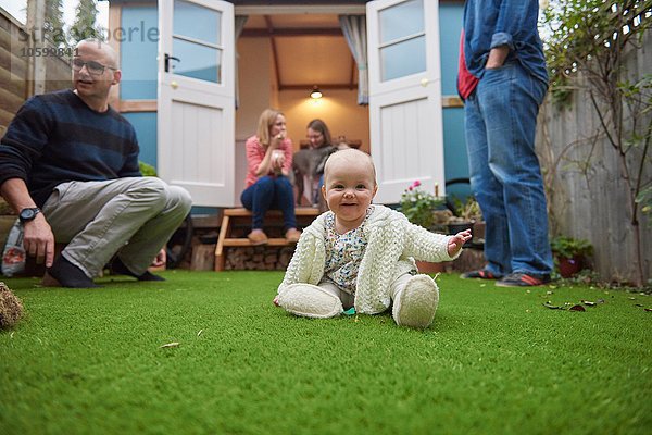 Kleines Mädchen im Garten auf Gras sitzend mit lächelndem Blick auf die Kamera