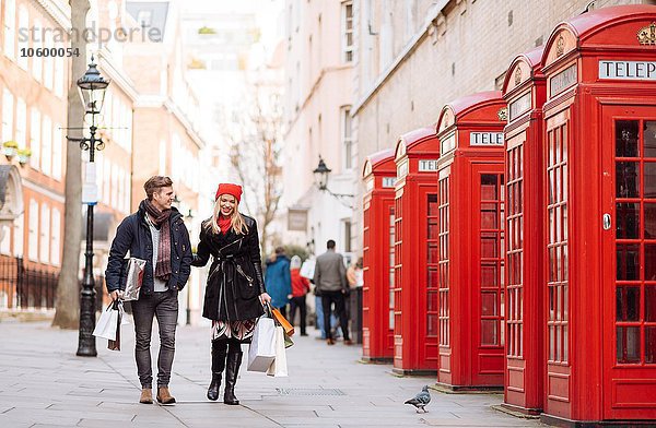 Junges Einkaufspaar schlendert an roten Telefonzellen vorbei  London  UK