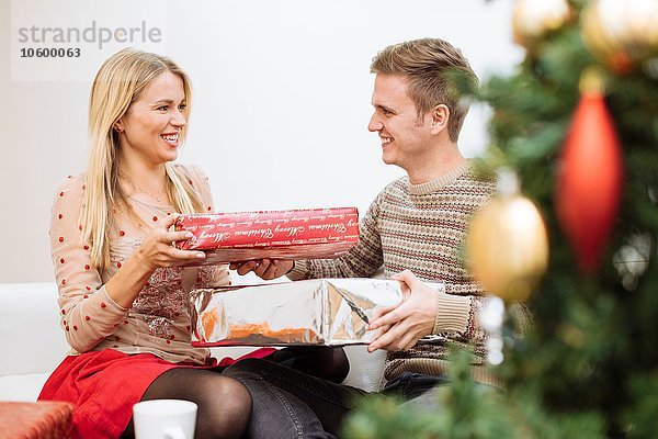 Junges Paar tauscht Weihnachtsgeschenke im Wohnzimmer aus