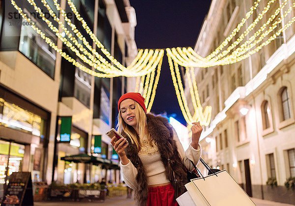 Junge Käuferin beim Lesen von Smartphone-Texten auf der Straße zu Weihnachten  London  UK