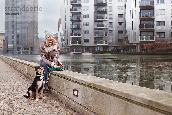 Mittlere erwachsene Frau und ihr Hund sitzen auf der Uferpromenade.