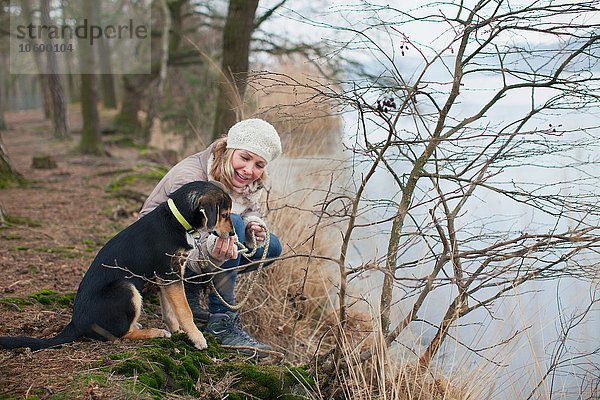 Mittlere erwachsene Frau kauernd mit ihrem Hund am Flussufer