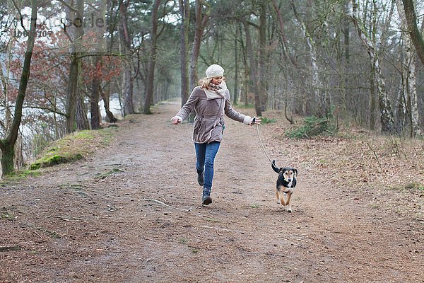 Mittlere erwachsene Frau  die mit ihrem Hund im Wald läuft.