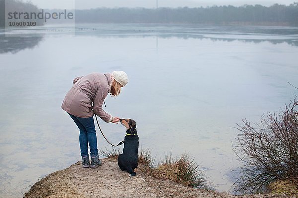 Mittlere erwachsene Frau  die ihren Hund am Flussufer streichelt.