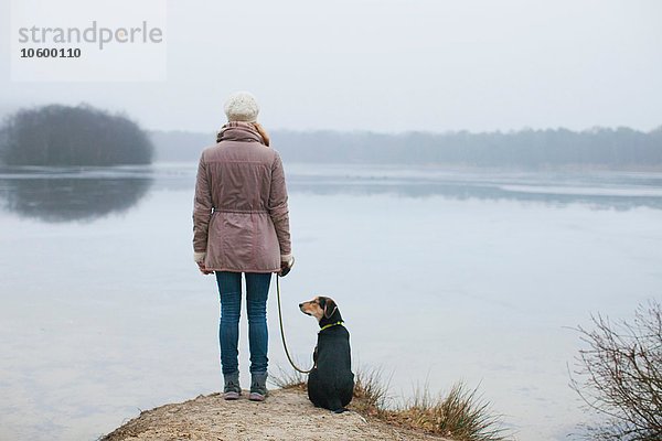 Rückansicht der Frau mit Hund vom Flussufer aus gesehen