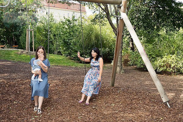 Junge Frau mit Mutter und Tochter auf Schaukeln im Park sitzend