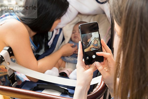 Junge Frau fotografiert Mutter und Tochter auf dem Smartphone