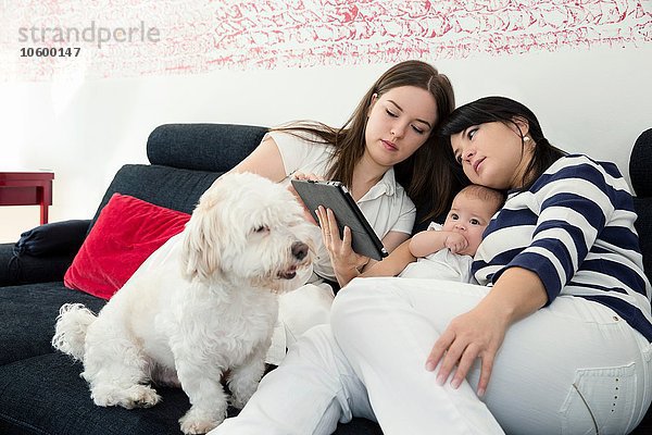Reife Frau und Tochter mit Baby-Mädchen beim Lesen des digitalen Tabletts auf dem Sofa