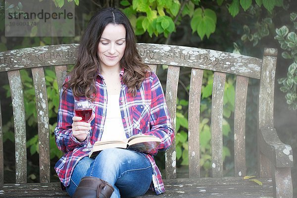 Mittlere erwachsene Frau beim Lesen und Trinken von Rotwein auf der Gartenbank im Thornbury Castle  South Gloucestershire  UK