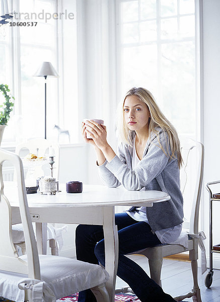 Junge Frau sitzt am Tisch und hält eine Tasse Kaffee
