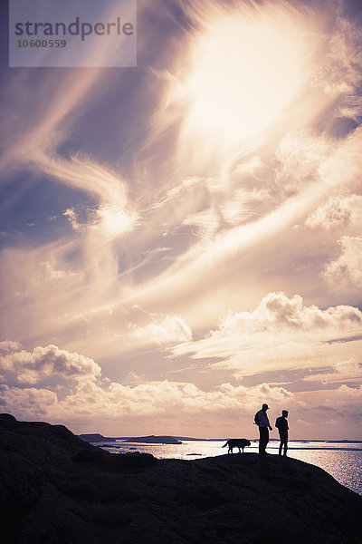 Silhouette von Männern mit Hund auf einer Klippe am Meer