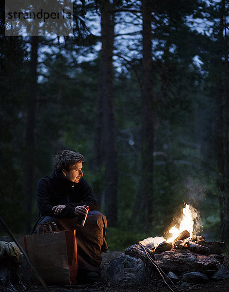 Mann sitzt am Holzfeuer im Wald