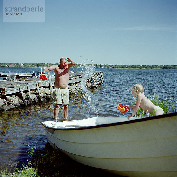 Mädchen bespritzt Großvater im See mit Wasser