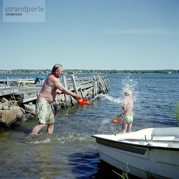 Großvater bespritzt ein Mädchen im See mit Wasser