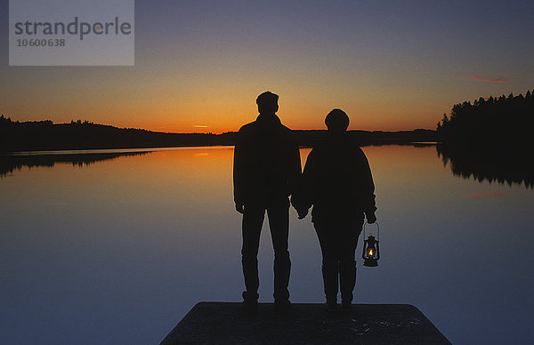 Ein Paar steht bei Sonnenuntergang auf einem Steg  Schweden.