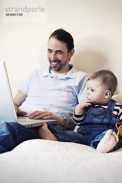 Mann mit Laptop und Baby neben sich