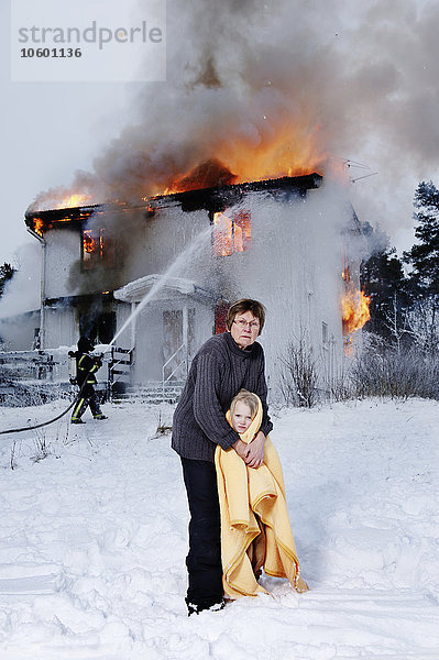 Großmutter hält gerettetes Mädchen  brennendes Gebäude im Hintergrund