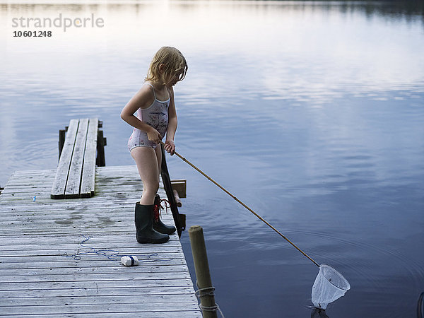 Mädchen steht mit Fischernetz auf dem Steg