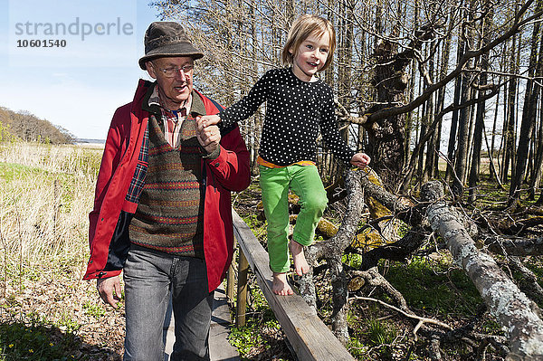 Großvater hilft seiner Enkelin  über den Zaun zu laufen