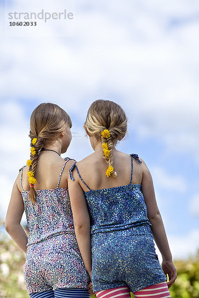 Zwei Mädchen mit Löwenzahnblüten in Zöpfen