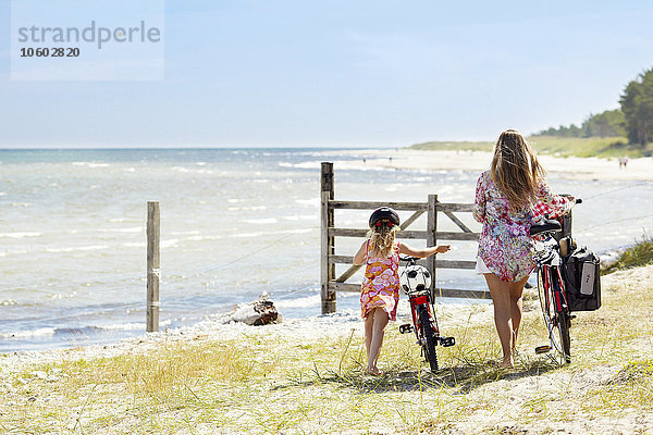 Mutter mit Tochter mit Fahrrädern am Meer
