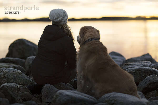 Frau mit Hund schaut in den Sonnenuntergang
