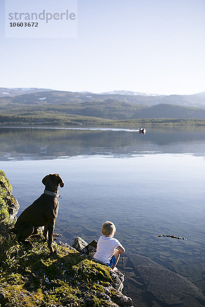 Junge mit Hund an der Küste sitzend