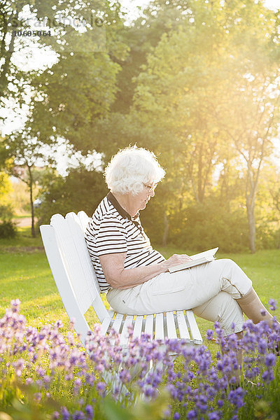 Ältere Frau liest ein Buch im Garten