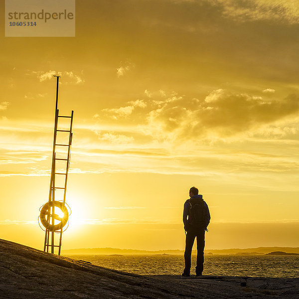 Mann beobachtet Sonnenuntergang am Meer
