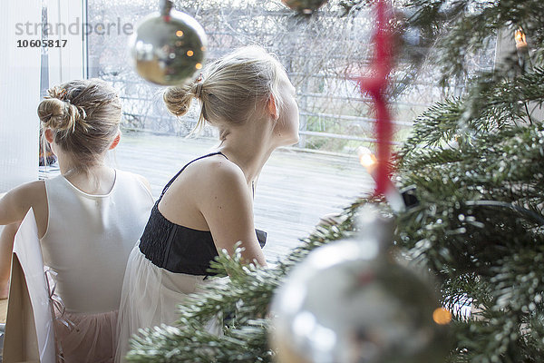 Mädchen schauen durch ein Fenster  Weihnachtsbaum im Vordergrund